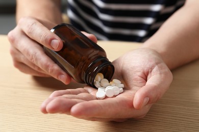 Man pouring pills from bottle at wooden table, closeup