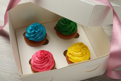 Box with delicious colorful cupcakes and ribbon on white wooden table, closeup
