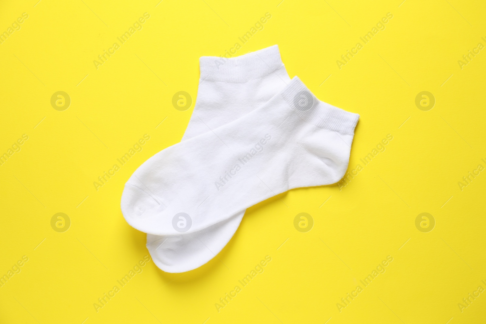 Photo of Pair of white socks on yellow background, flat lay