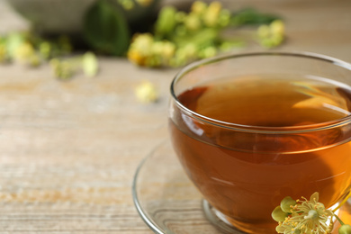 Photo of Cup of tea and linden blossom on wooden table, closeup. Space for text