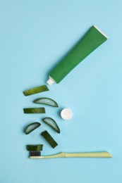 Tube of toothpaste, toothbrush and fresh cut aloe on light blue background, flat lay