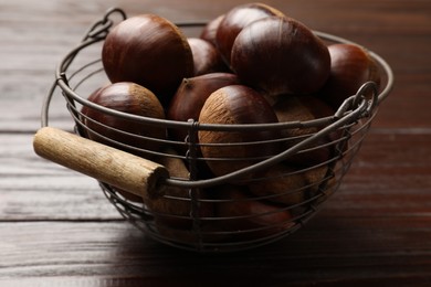 Photo of Sweet fresh edible chestnuts in metal basket on wooden table, closeup
