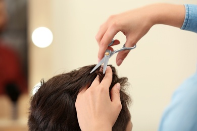 Photo of Barber making stylish haircut with professional scissors in beauty salon, closeup