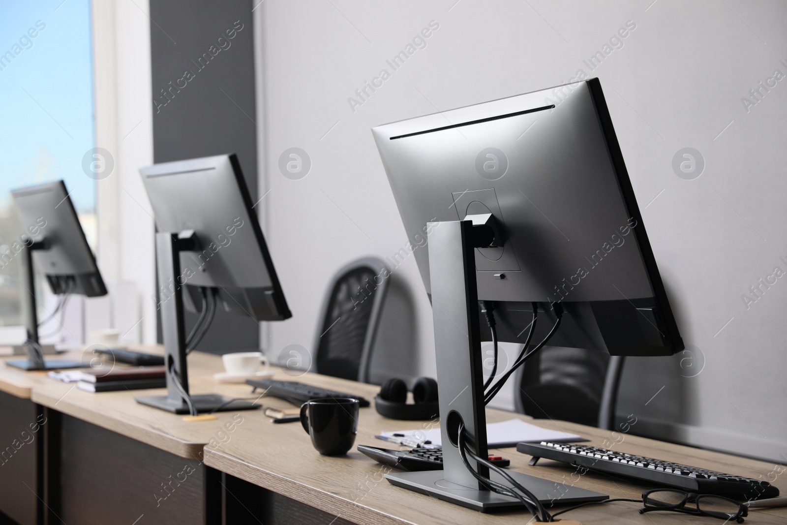 Photo of Open office interior. Modern workplaces with computers near light grey wall