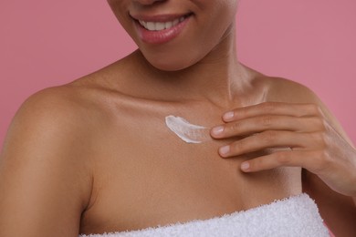 Young woman applying cream onto body on pink background, closeup