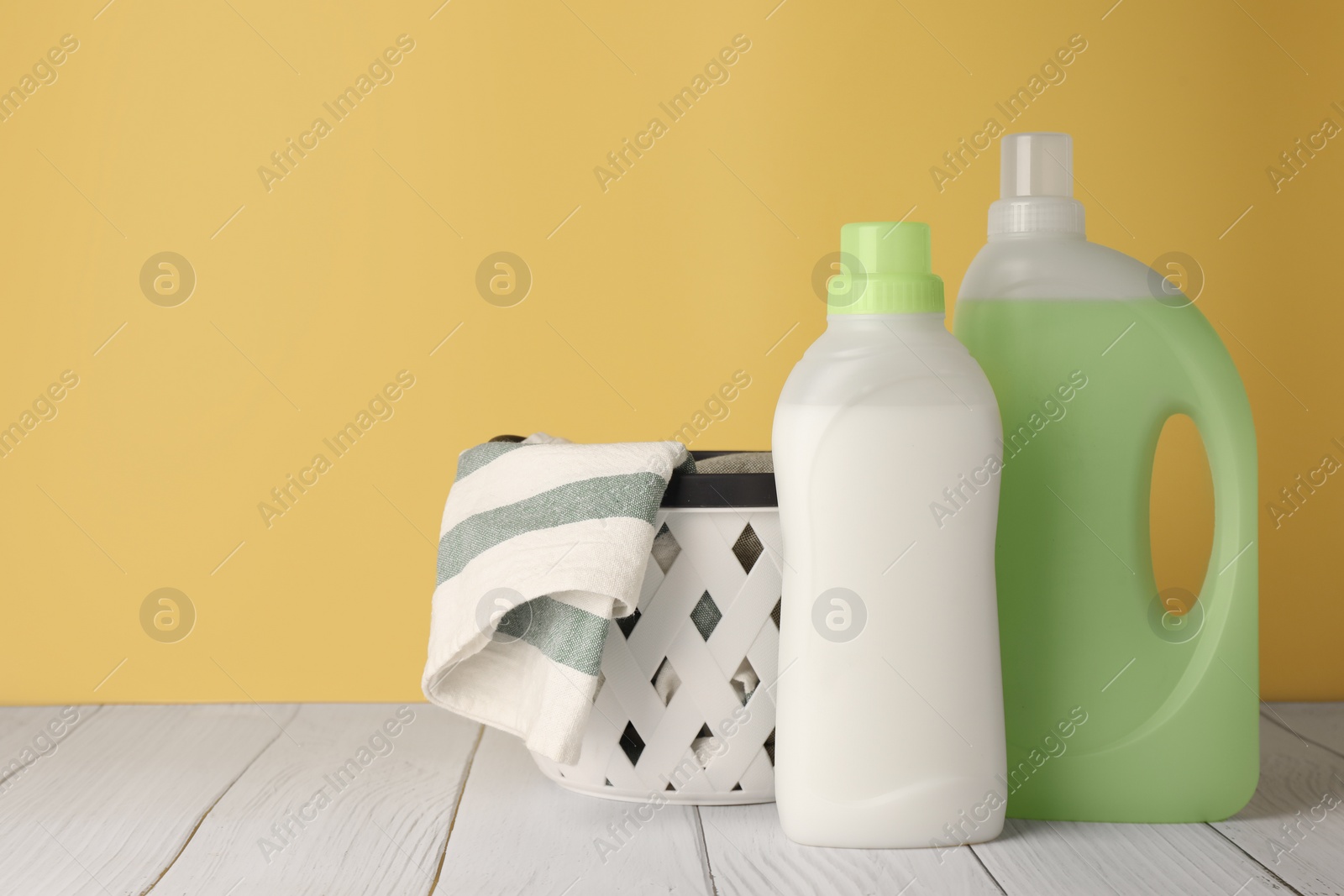 Photo of Bottles of fabric softener and towels in basket on white wooden table, space for text