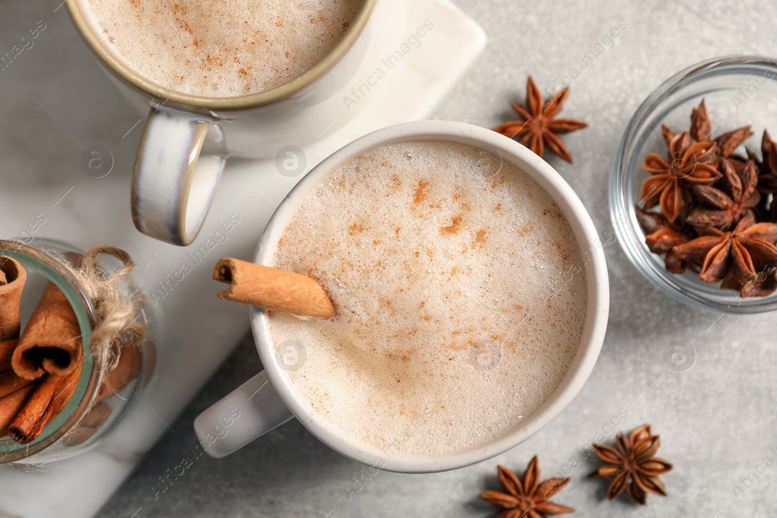 Photo of Cups of delicious eggnog with anise and cinnamon on light grey table, flat lay