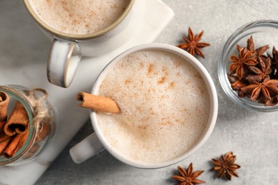 Photo of Cups of delicious eggnog with anise and cinnamon on light grey table, flat lay