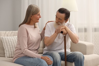 Photo of Senior man with walking cane and mature woman on sofa at home