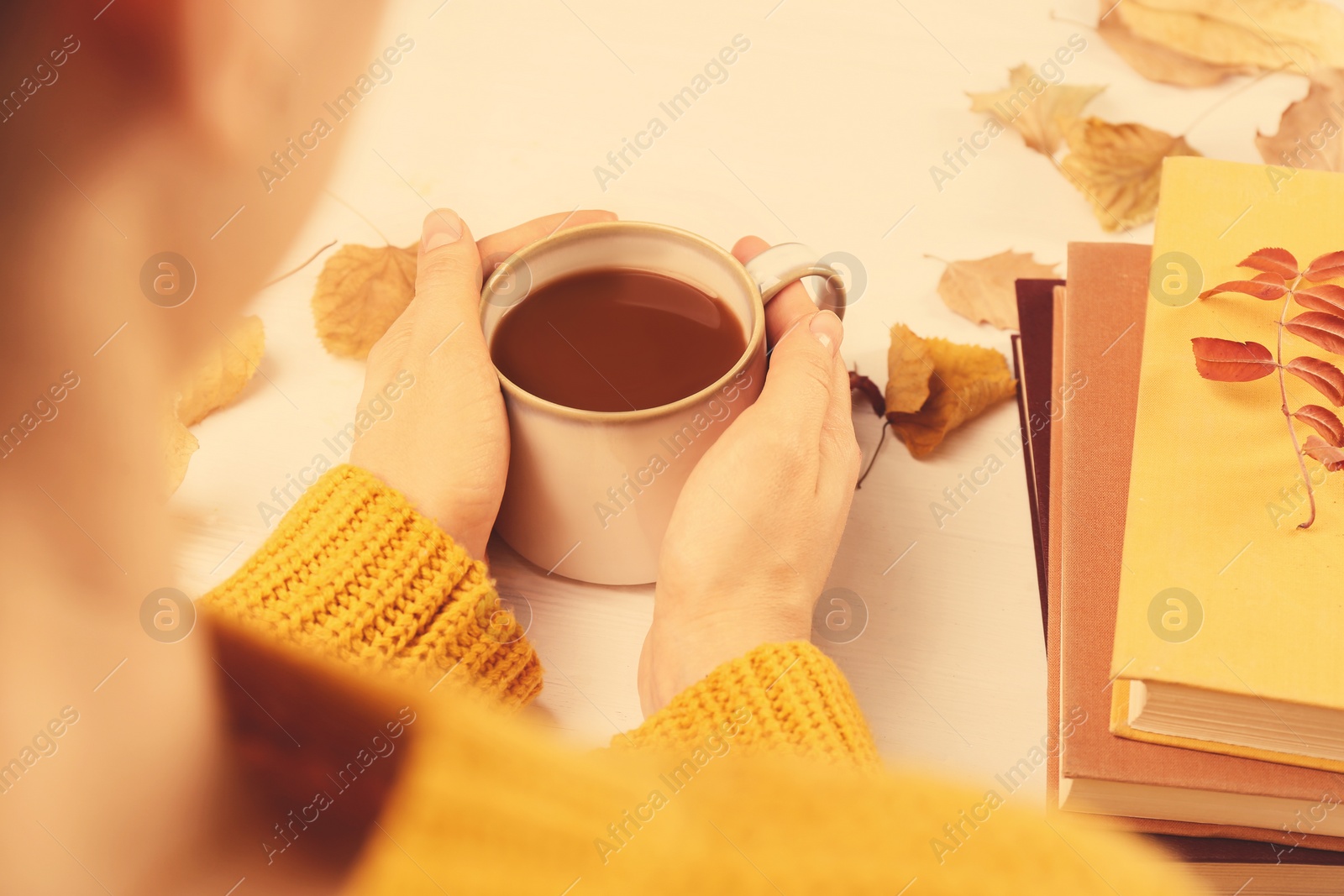 Photo of Woman with cup of hot drink at white wooden table, closeup. Cozy autumn atmosphere