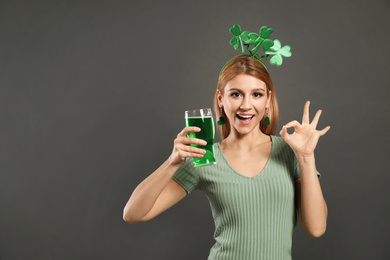 Young woman with clover headband and green beer on grey background, space for text. St. Patrick's Day celebration