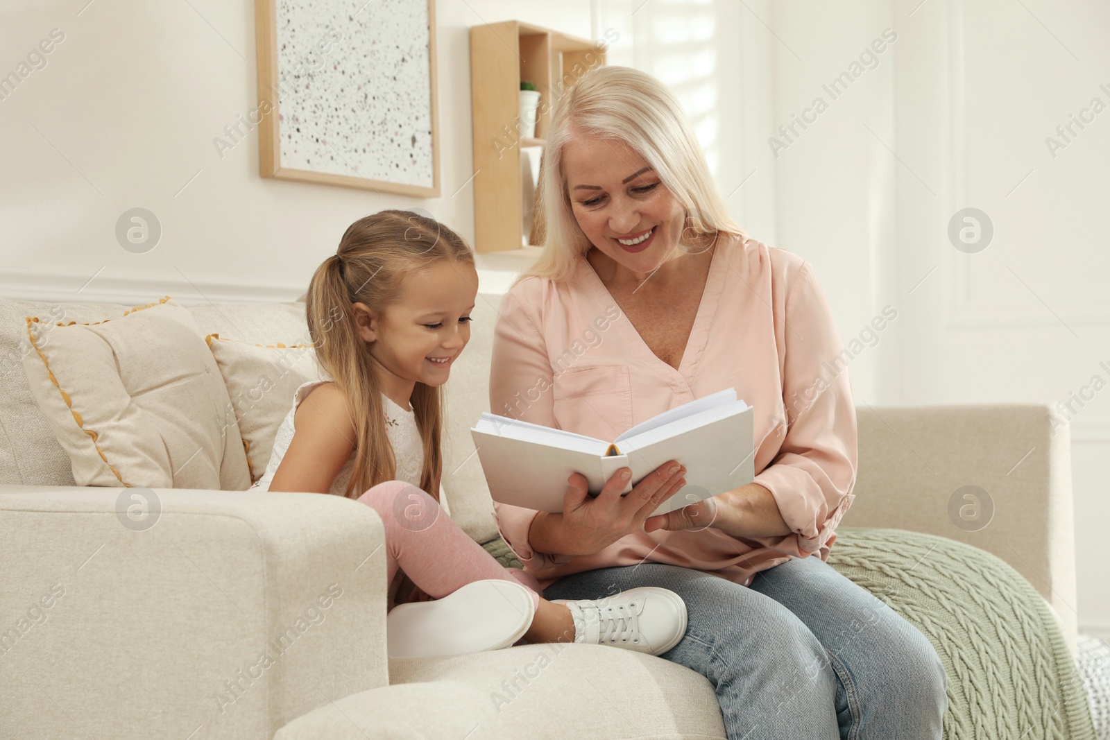 Photo of Happy grandmother with her granddaughter reading book together at home