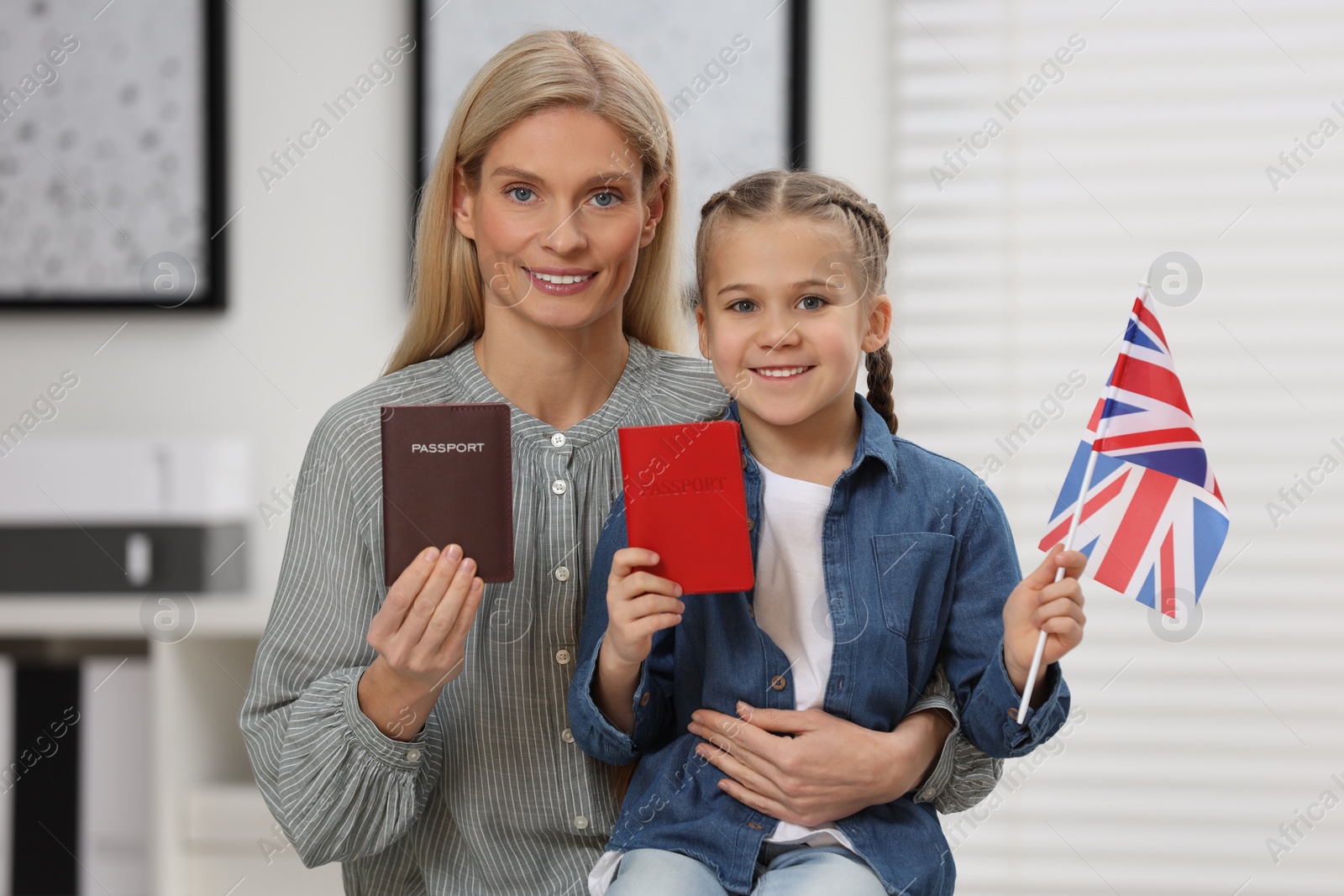 Photo of Immigration. Happy woman with her daughter holding passports and flag of United Kingdom indoors