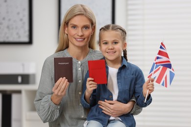 Immigration. Happy woman with her daughter holding passports and flag of United Kingdom indoors