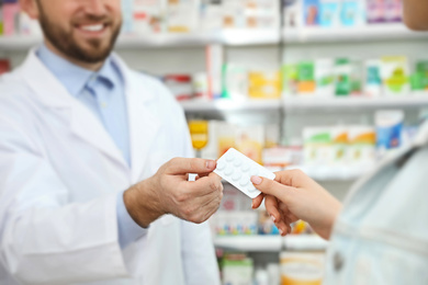 Professional pharmacist giving pills to customer in modern drugstore, closeup