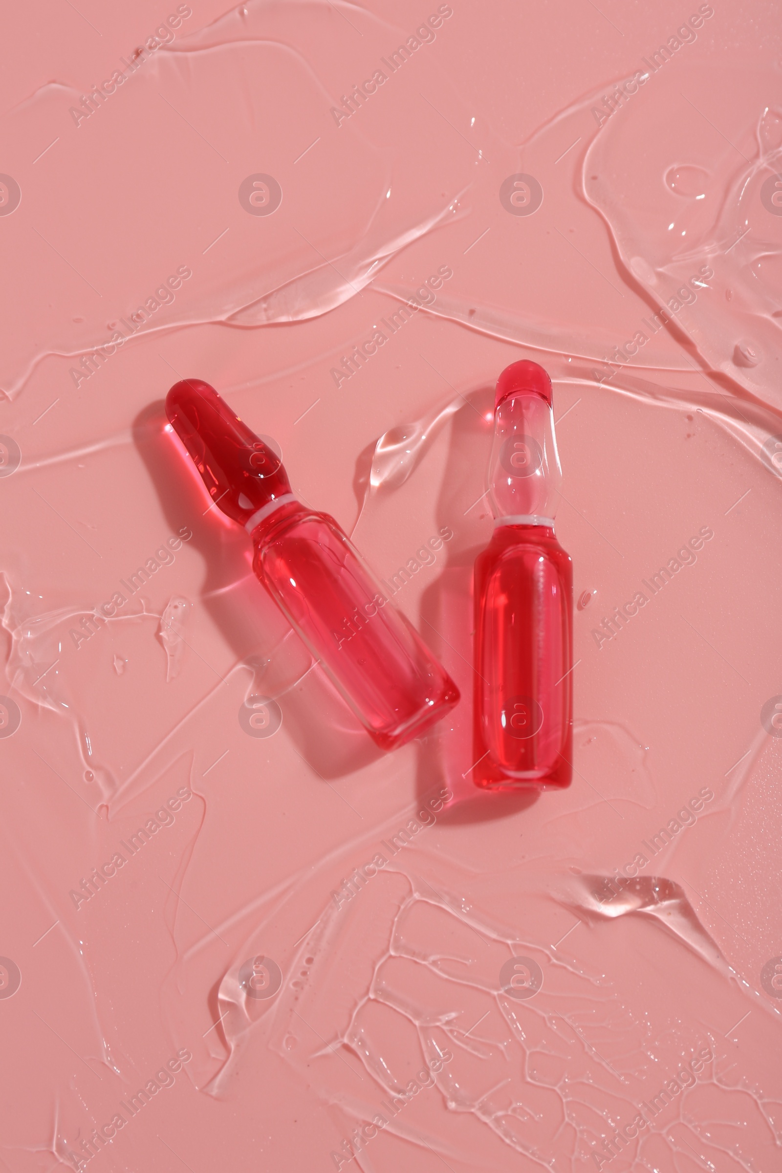 Photo of Skincare ampoules on pink surface with gel, top view