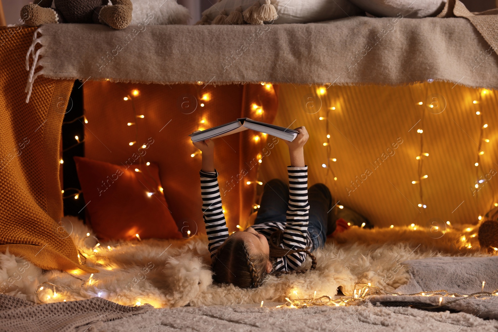 Photo of Girl reading book in decorated play tent at home