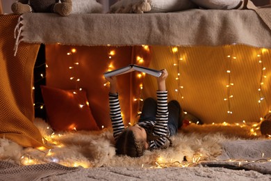 Photo of Girl reading book in decorated play tent at home