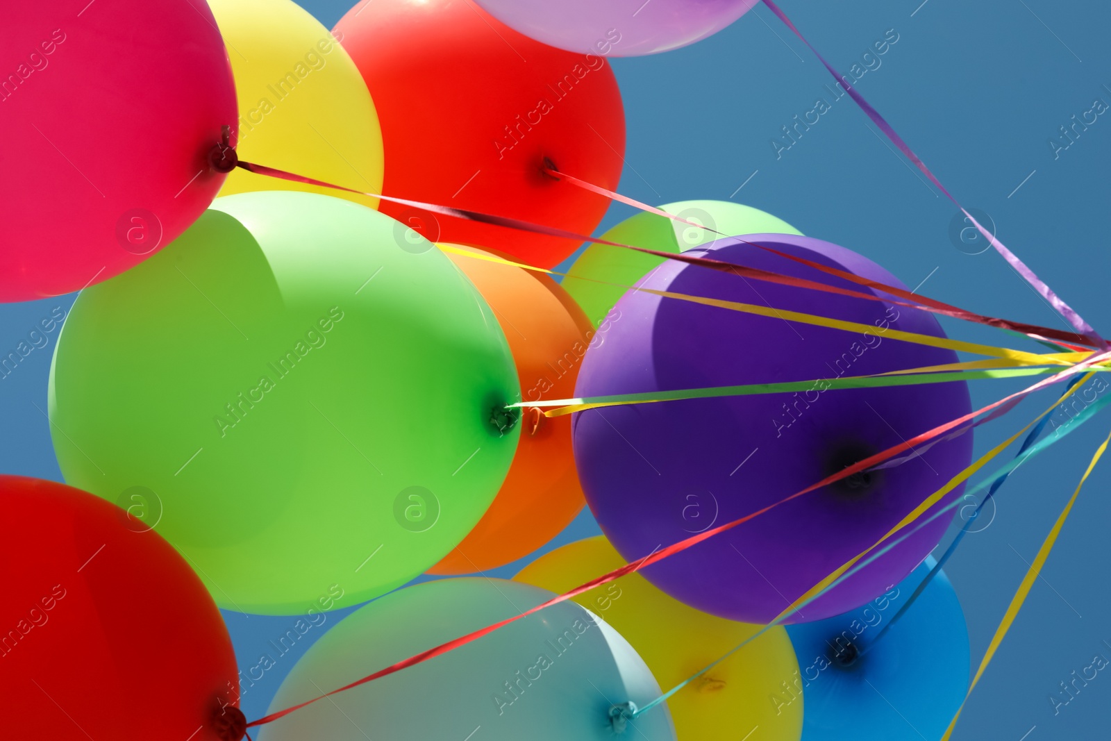 Photo of Bunch of colorful balloons against blue sky, bottom view