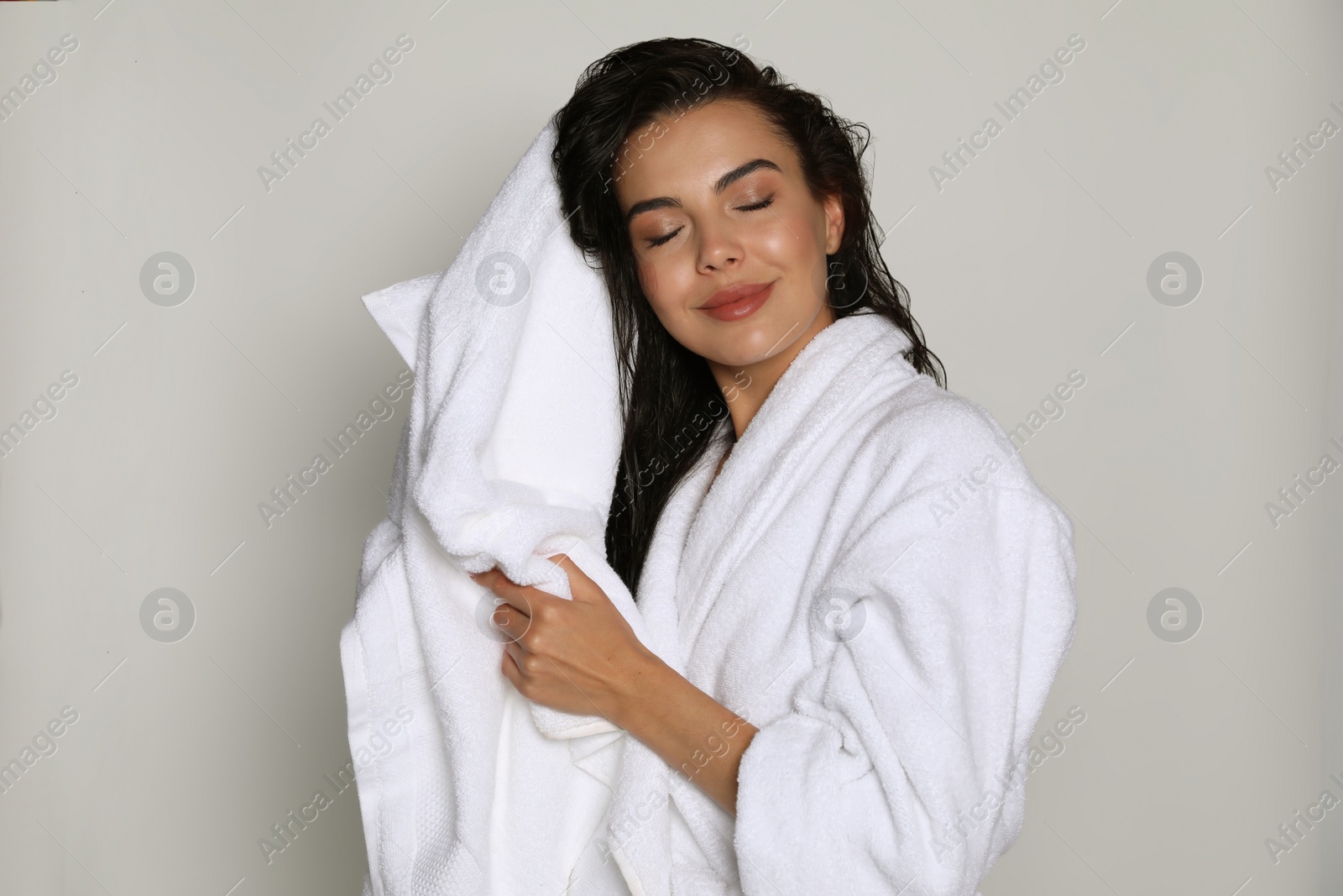 Photo of Beautiful young woman in bathrobe drying hair with towel on light background