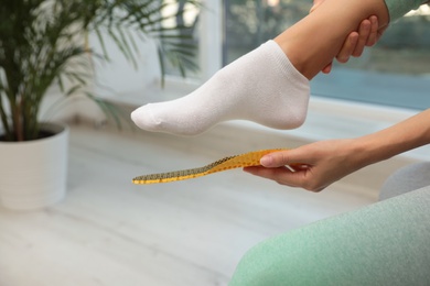 Photo of Woman fitting orthopedic insole indoors, closeup. Foot care