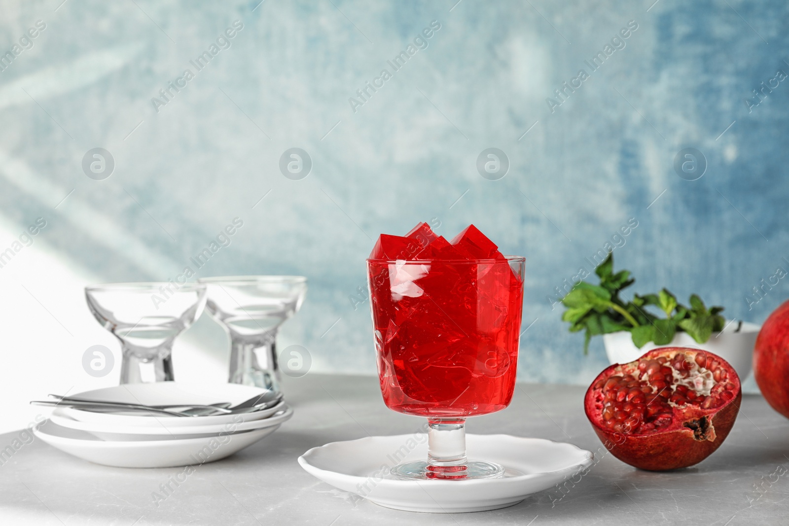 Photo of Composition with glass of pomegranate jelly on table against color background. Space for text