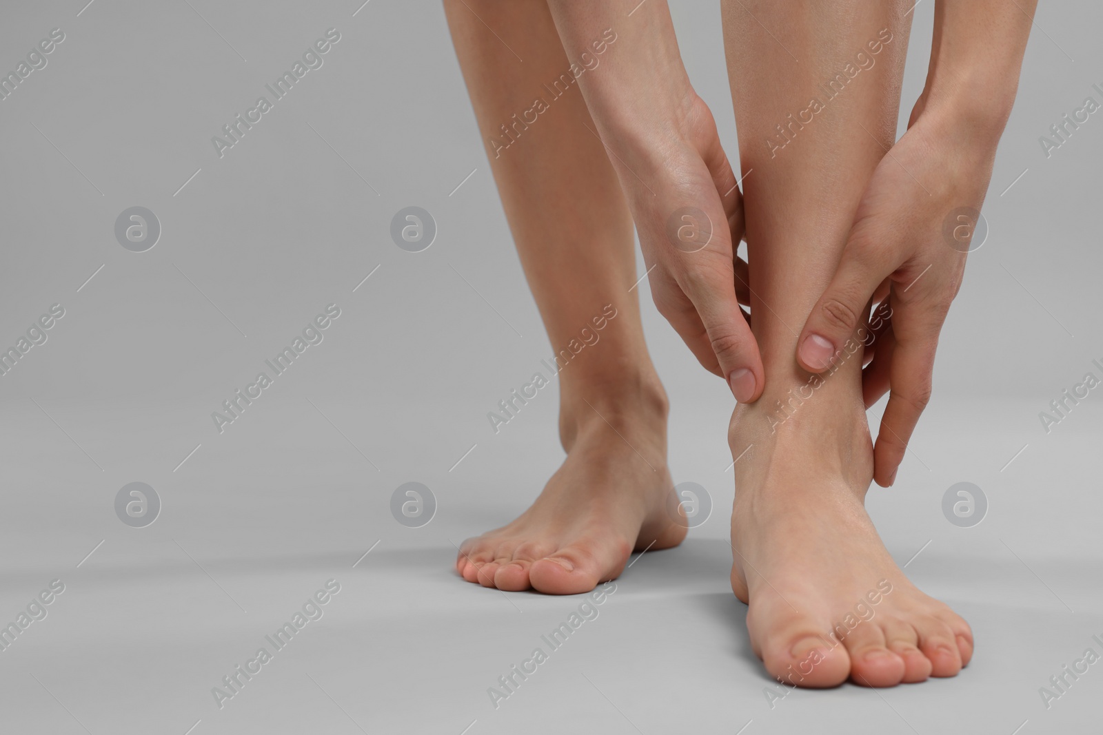 Photo of Woman suffering from leg pain on grey background, closeup. Space for text