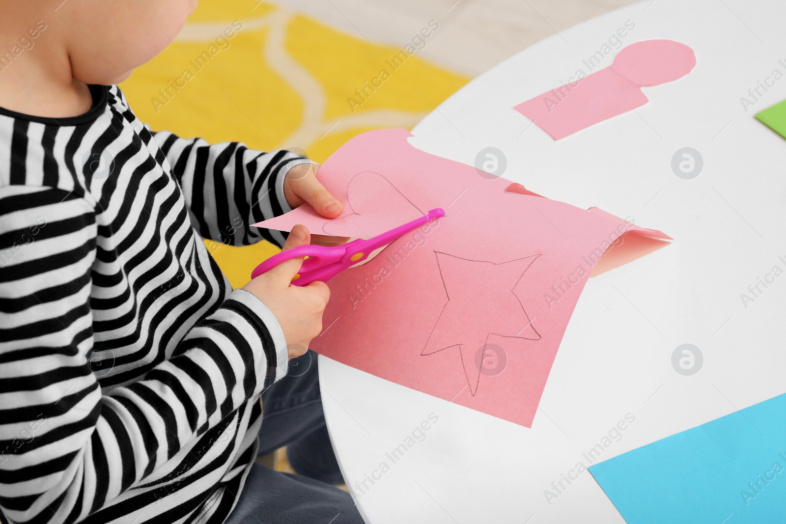 Photo of Girl cutting pink paper at desk in room, closeup. Home workplace