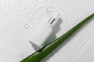 Photo of Bottle of cosmetic product and aloe leaf in water on white background, flat lay