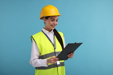 Engineer in hard hat holding clipboard on light blue background