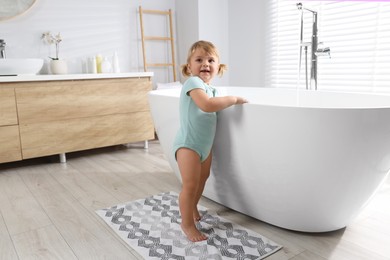 Photo of Curious little girl near tub in bathroom