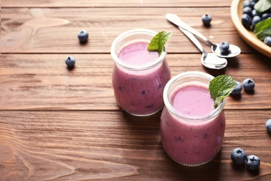 Photo of Tasty blueberry smoothie in jars, berries and space for text on wooden table