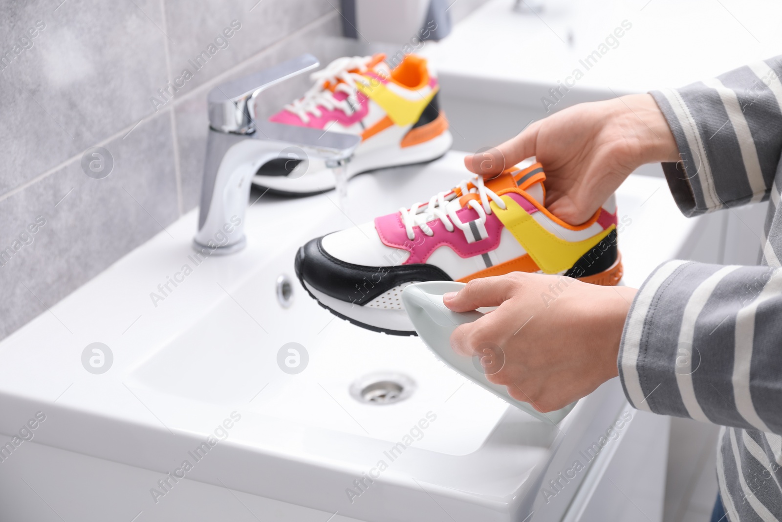 Photo of Woman washing stylish sneakers with brush in sink, closeup