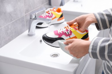 Woman washing stylish sneakers with brush in sink, closeup