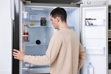 Photo of Man near empty refrigerator in kitchen at home
