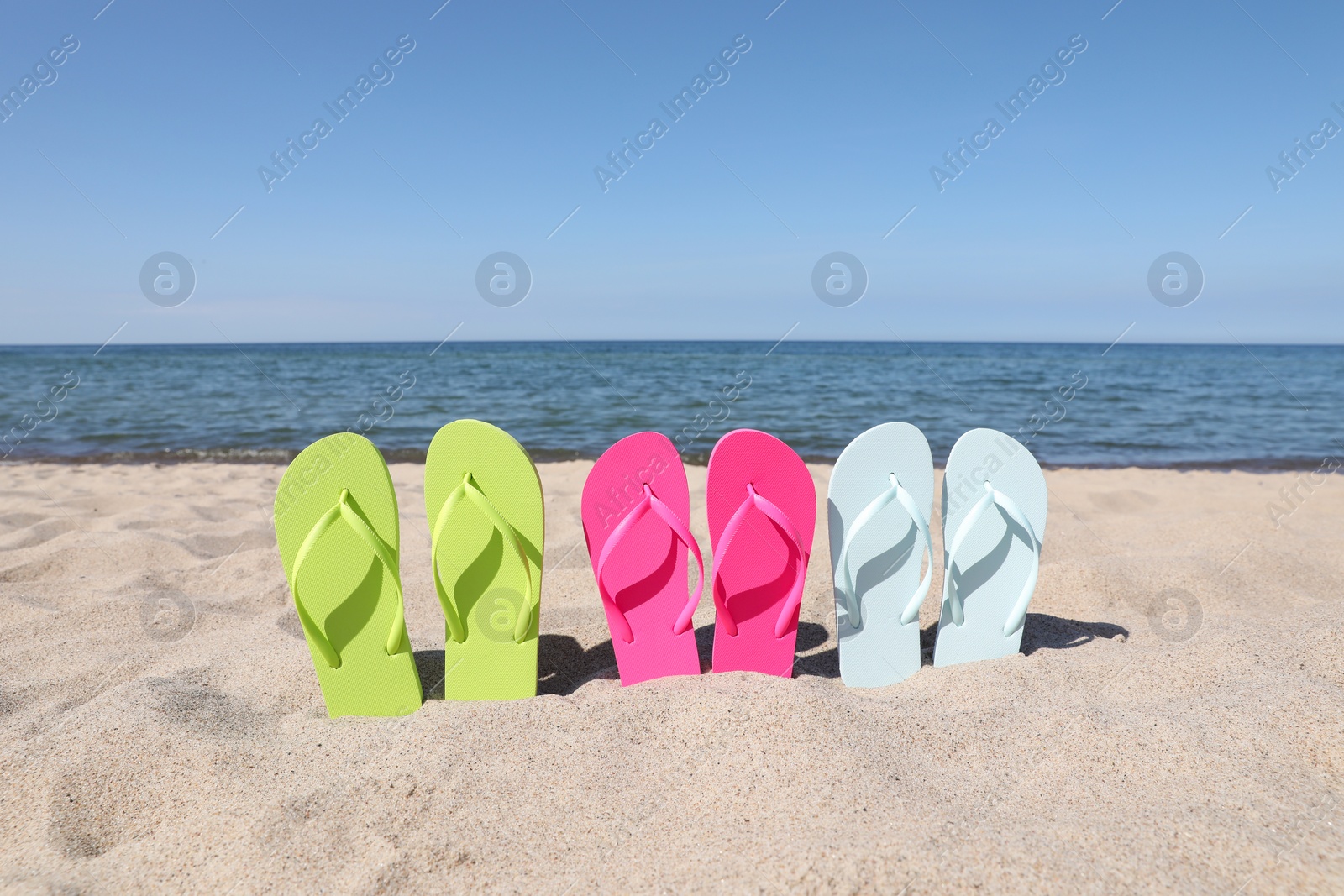 Photo of Stylish colorful flip flops on beach sand