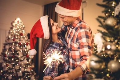Photo of Couple holding sparklers in room decorated for Christmas