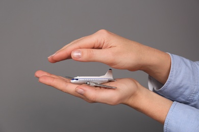 Insurance agent covering toy plane on grey background, closeup. Travel safety concept