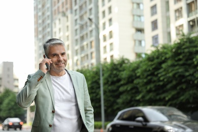 Photo of Handsome mature man talking on phone in city center. Space for text