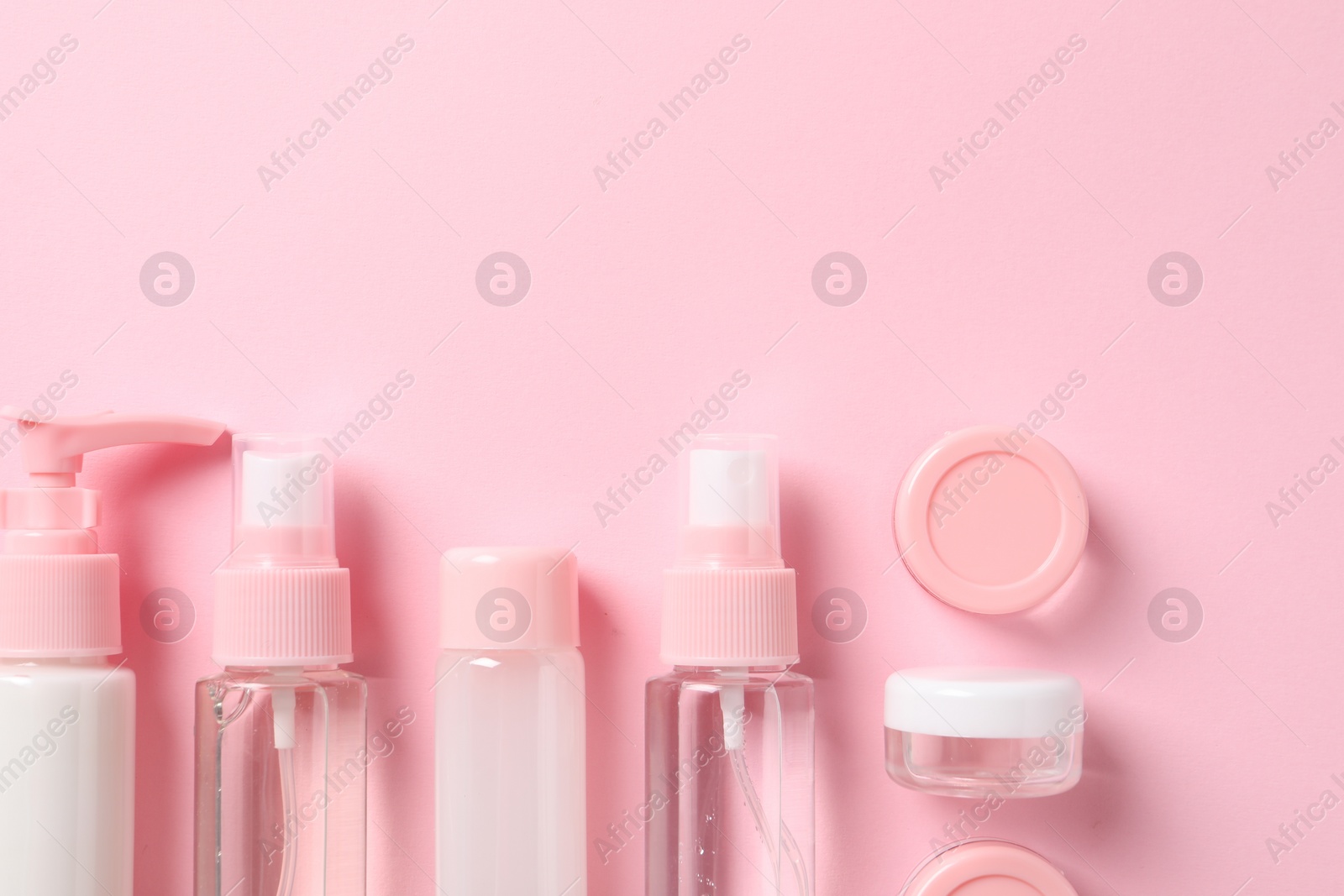 Photo of Cosmetic travel kit on pink background, flat lay. Space for text