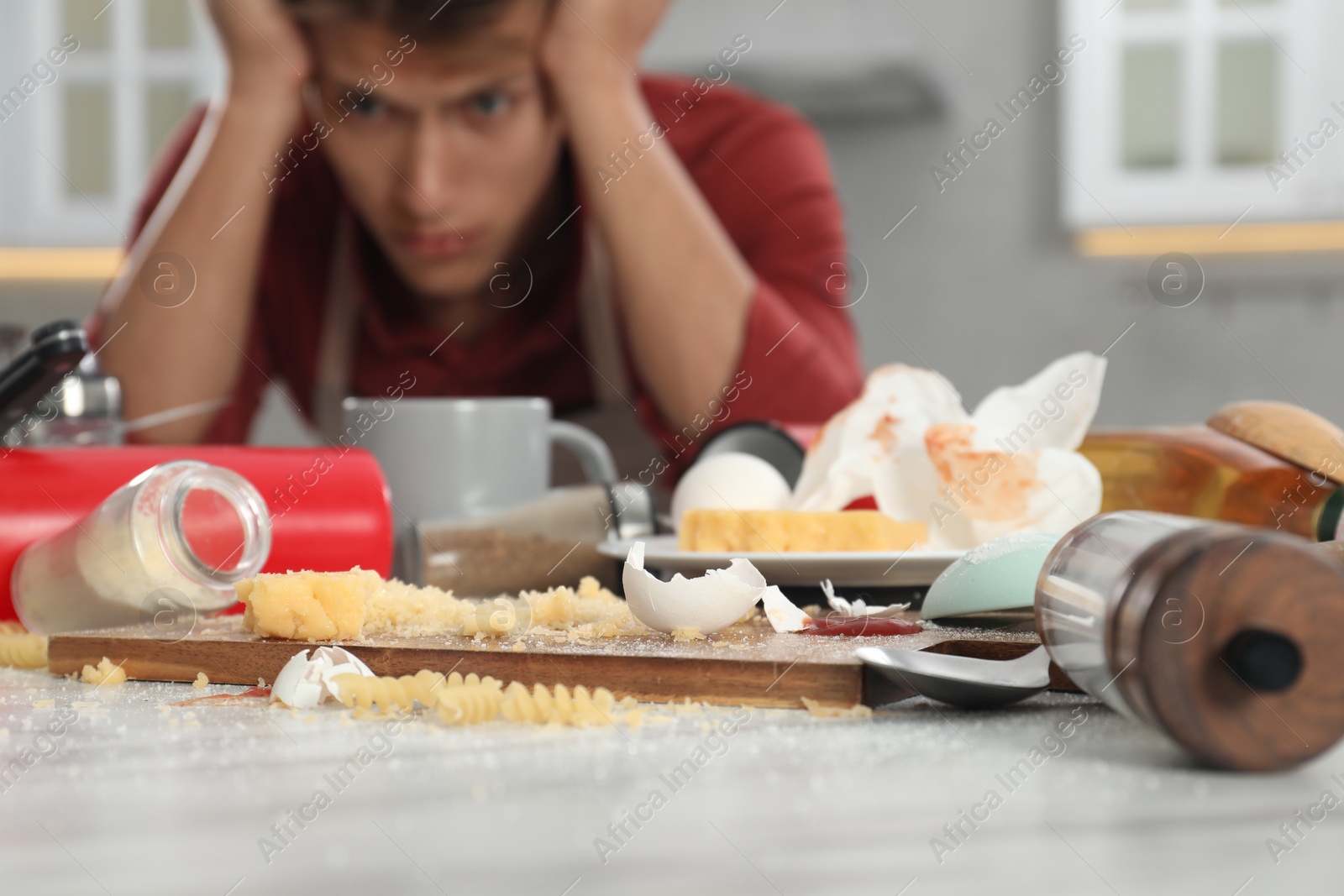 Photo of Stressed man in messy kitchen. Many dirty dishware, utensils and food leftovers on table, selective focus
