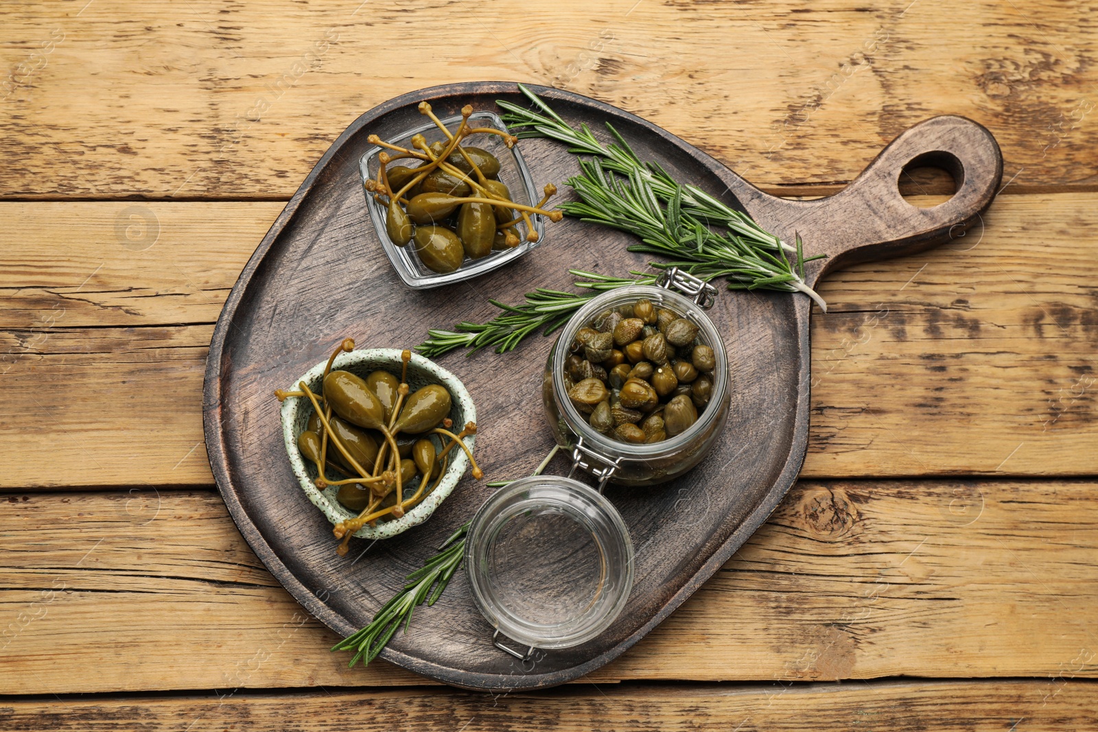 Photo of Delicious pickled capers and rosemary twigs on wooden table, top view