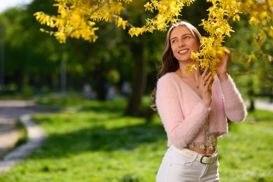 Photo of Beautiful young woman near blossoming shrub on spring day, space for text