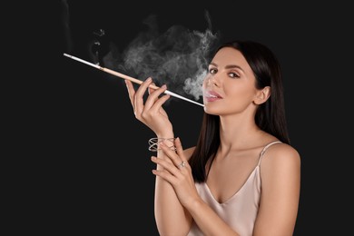 Woman using long cigarette holder for smoking on black background, space for text