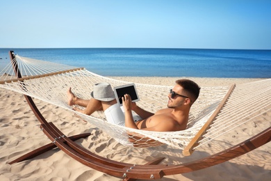 Young man with tablet in hammock on beach