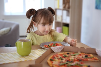 Photo of Cute little girl eating tasty pizza at home