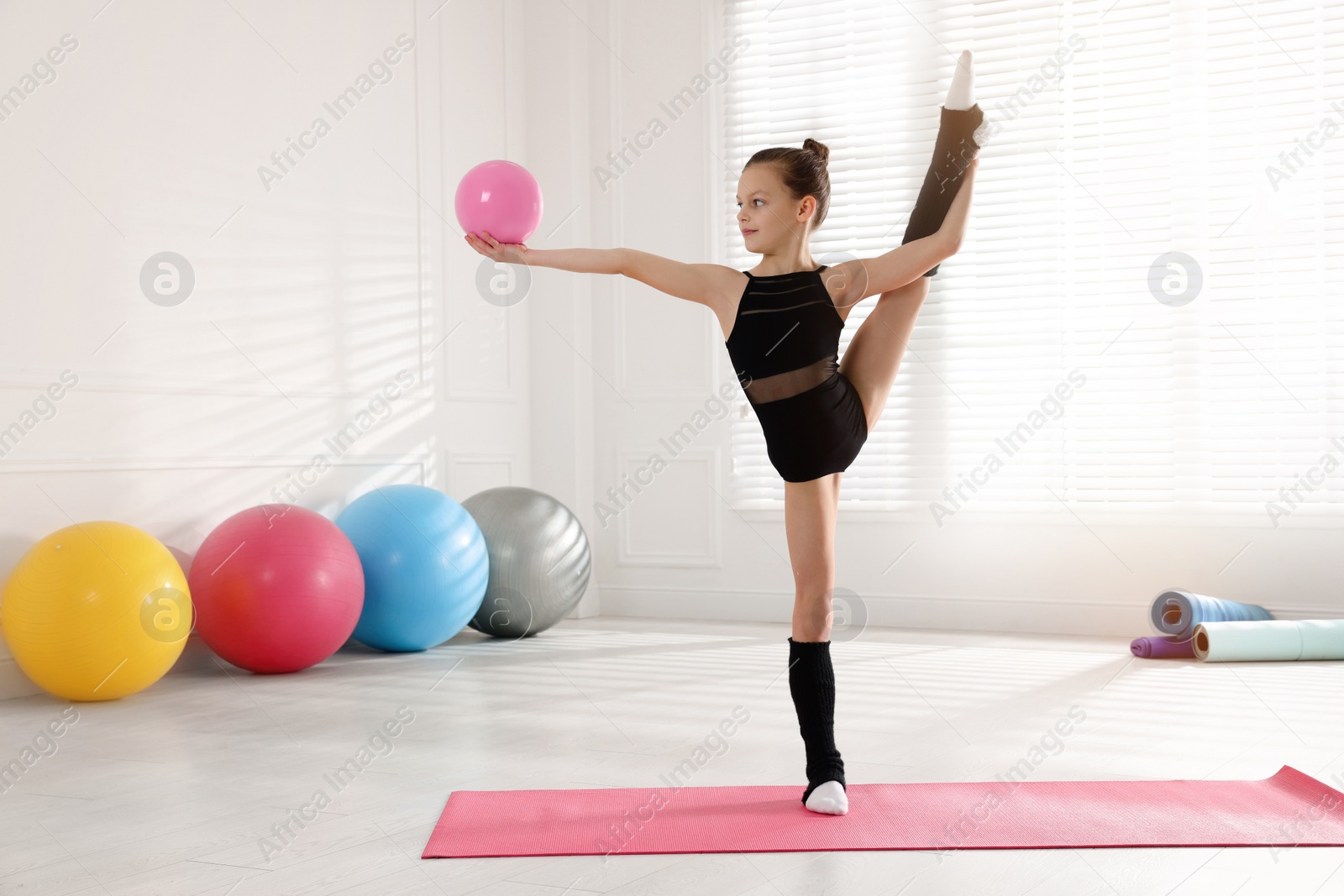 Photo of Cute little gymnast with ball doing standing split indoors