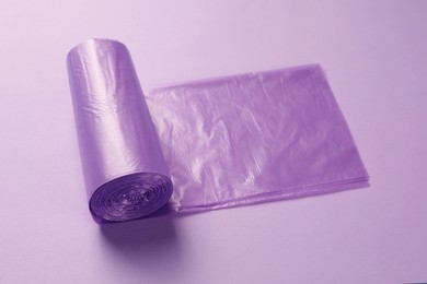 Photo of Roll of violet garbage bags on color background. Cleaning supplies