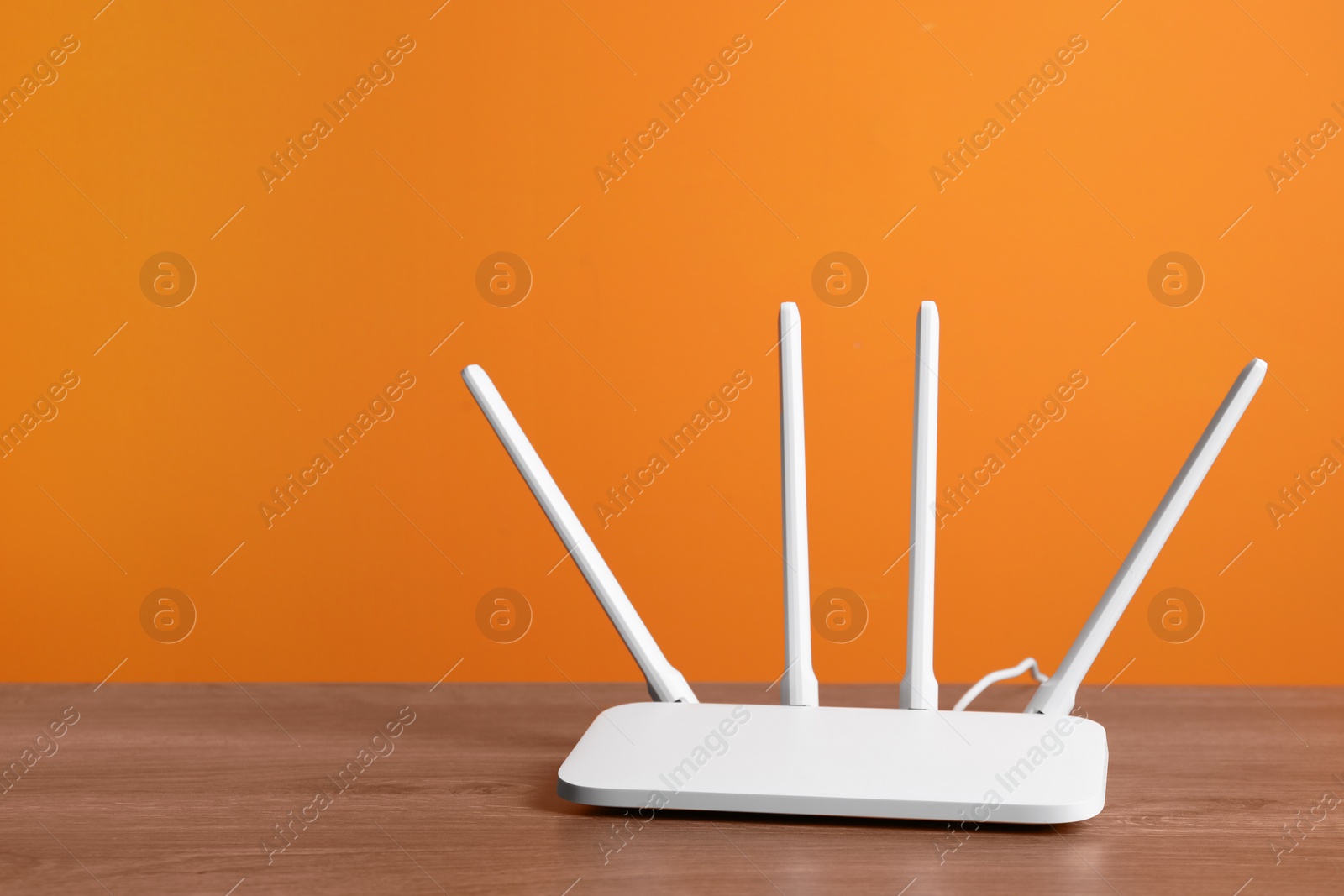 Photo of New modern Wi-Fi router on wooden table near orange wall, space for text
