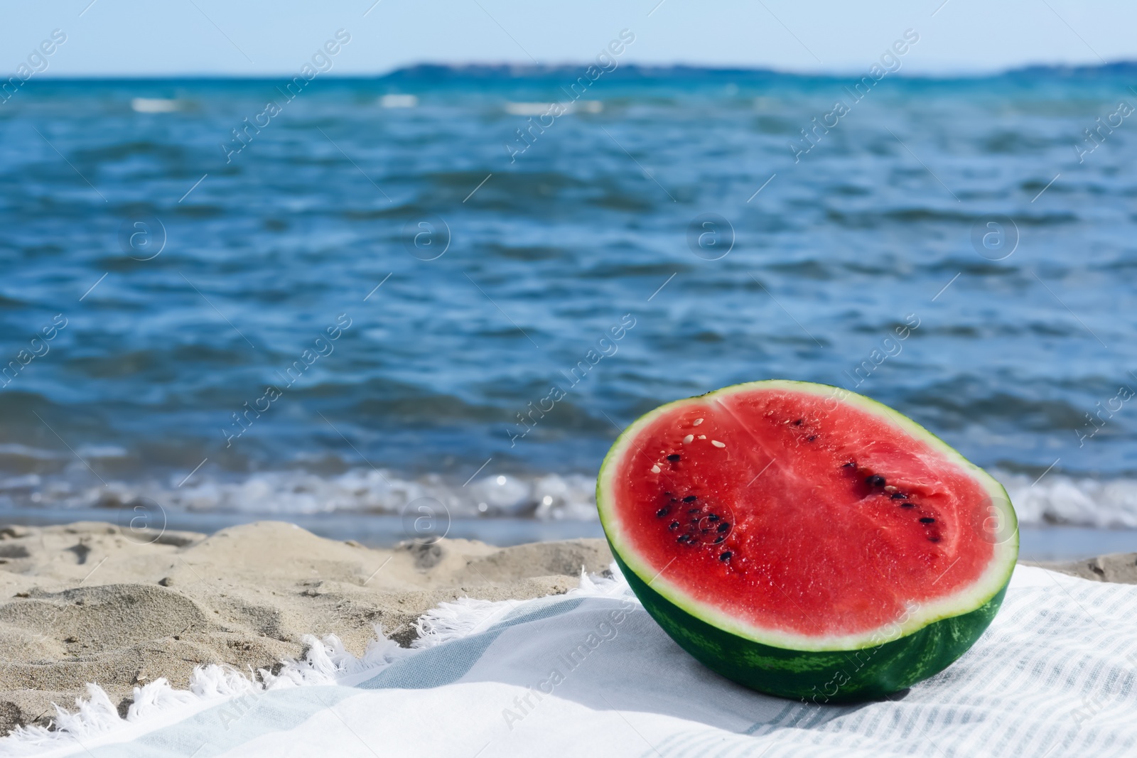 Photo of Half of fresh juicy watermelon on beach blanket near sea, space for text